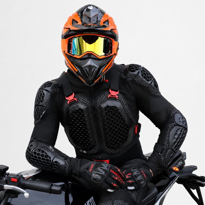 A person wearing a black full-face motorcycle helmet with an orange visor, black protective armor jacket, matching gloves, and a black riding suit, seated on a motorcycle against a light gray studio background.