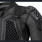 Close-up of a black protective sports jacket showing the shoulder, upper chest, and back panels with breathable mesh and hard shell protection.