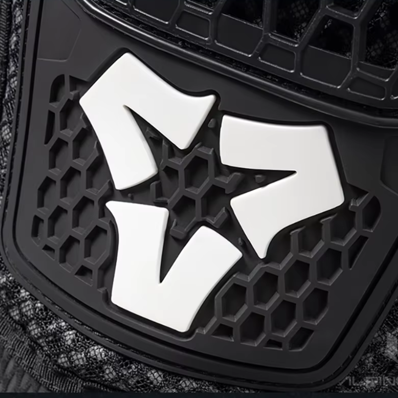 A close-up of a black honeycomb-patterned protective panel with a textured dark fabric visible along the lower left edge.
