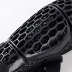 Close-up of a black protective sports guard with a honeycomb ventilation pattern and textured grip details, shown against a plain light background.