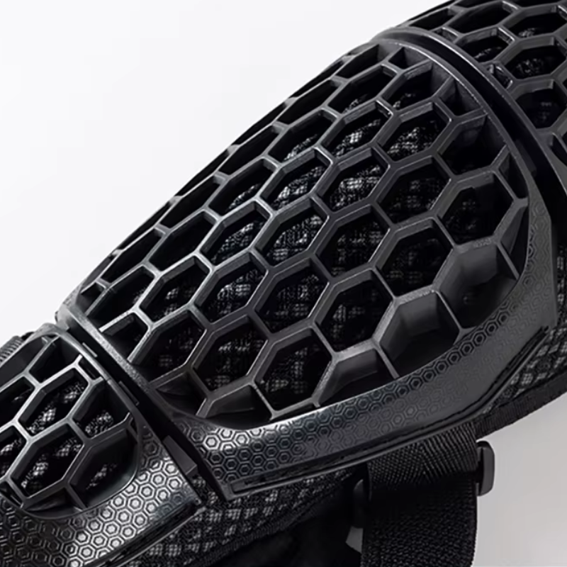 Close-up of a black protective sports guard with a honeycomb ventilation pattern and textured grip details, shown against a plain light background.