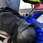 Close-up of a person wearing black motorcycle knee and hip protective armor while sitting on a blue motorcycle.