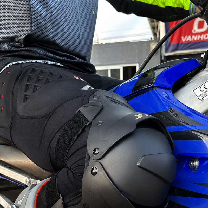 Close-up of a person wearing black motorcycle knee and hip protective armor while sitting on a blue motorcycle.