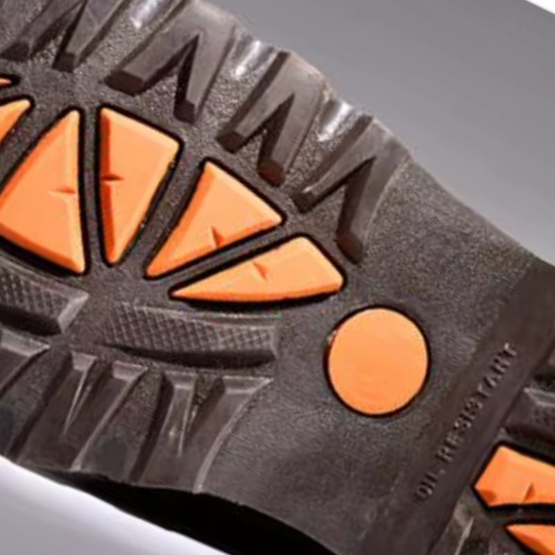 Close-up of a black rubber shoe sole with bright orange triangular and circular tread details, showing the 'OIL RESISTANT' text molded into the rubber.