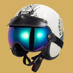 A white retro-style motorcycle helmet with black leather visor and straps, featuring a large mirrored blue-purple visor and decorative black graphics on the side, set against a solid tan background.