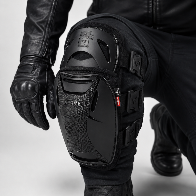 Black motorcycle knee protector with integrated gloves and pants, shown on a model in a crouching position against a light gray studio background.