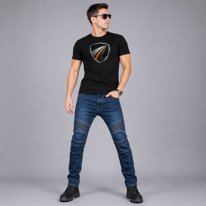A man wearing a black short-sleeve t-shirt with a metallic shield Bonny's  logo on the chest, paired with blue denim jeans and black boots, standing against a solid gray studio background.