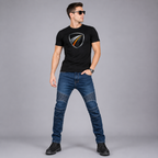 A man wearing a black short-sleeve t-shirt with a metallic shield Bonny's  logo on the chest, paired with blue denim jeans and black boots, standing against a solid gray studio background.