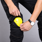 A close-up of a person wearing black ribbed knee-high compression sleeves or pants cuffs, pulling a bright yellow protective pad 
