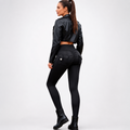 A woman shown from the back wearing a black faux-leather cropped jacket, black high-waisted ruched leggings with a side pocket, and black ankle boots, against a light gray studio background.