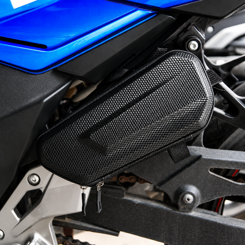A black carbon-fiber-pattern motorcycle side bag mounted on the side of a blue and black motorcycle.