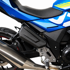 Close-up of a blue and black motorcycle showing the side panel, seat, exhaust pipe, and engine components against a white studio background.