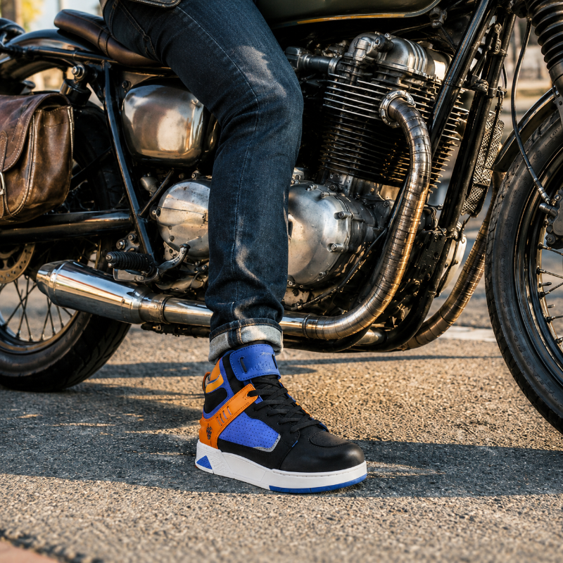 A person wearing a pair of black, blue, and orange high-top sneakers sits on a motorcycle on an asphalt road.