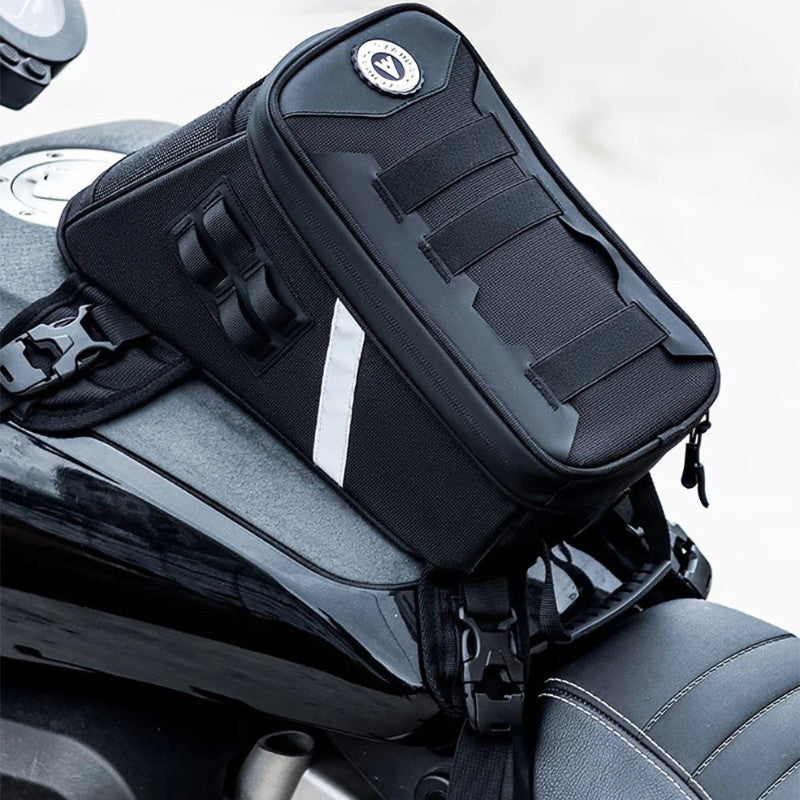 A black motorcycle tank bag with multiple zippered compartments and hook-and-loop straps, mounted on the seat of a black motorcycle.