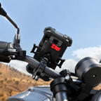A close-up of a black motorcycle handlebar mount holding a smartphone case, attached to the handlebars with a red release button, set against a blurred outdoor background of blue sky and hills.