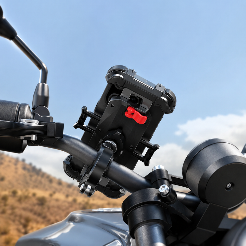 A close-up of a black motorcycle handlebar mount holding a smartphone case, attached to the handlebars with a red release button, set against a blurred outdoor background of blue sky and hills.