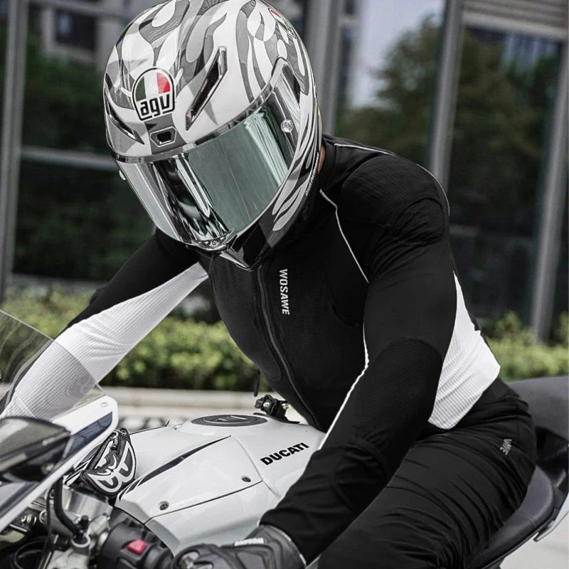 A person wearing a black and white riding jacket, black pants, and a white AGV full-face helmet with a clear visor, seated on a white Ducati motorcycle in an outdoor urban setting.