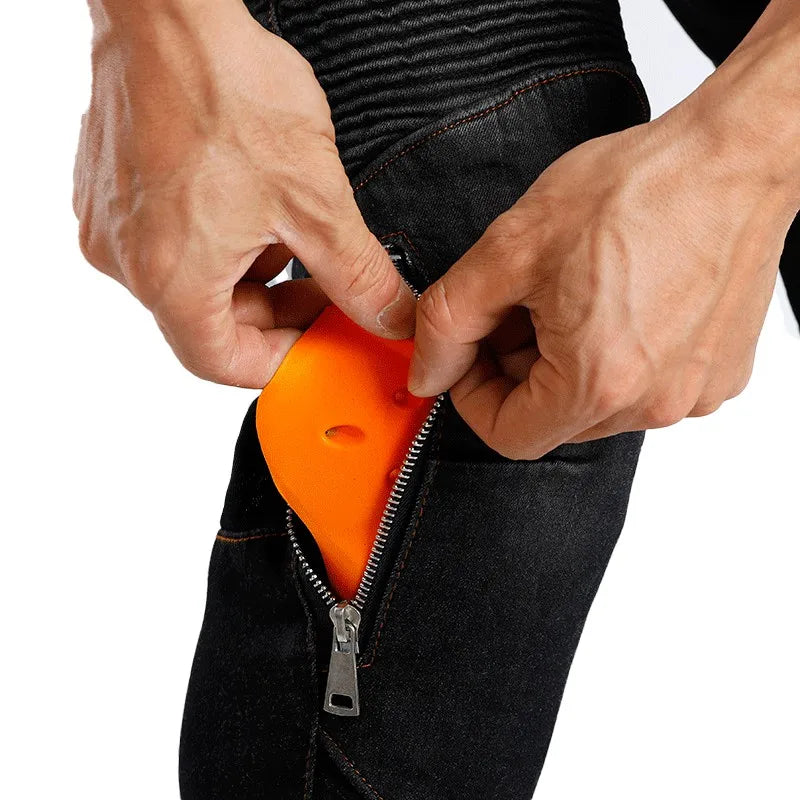 Close-up of a person's hands inserting a bright orange, zippered pouch into the pocket of black jeans against a white background.