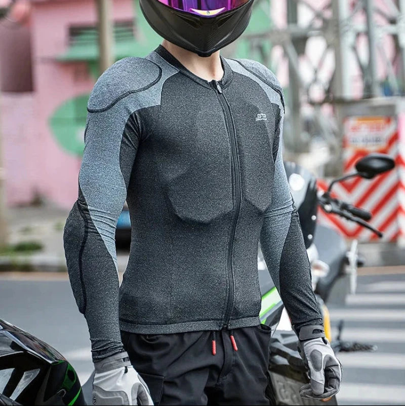 A person wearing a black full-face motorcycle helmet with a reflective purple-tinted visor, a dark gray long-sleeve technical riding jersey, and black gloves, standing outdoors near a motorcycle.