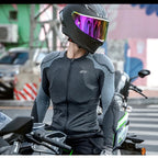 A person wearing a black full-face motorcycle helmet with a reflective visor and a dark gray long-sleeve zip-up riding jersey sits on a motorcycle in an outdoor urban setting.