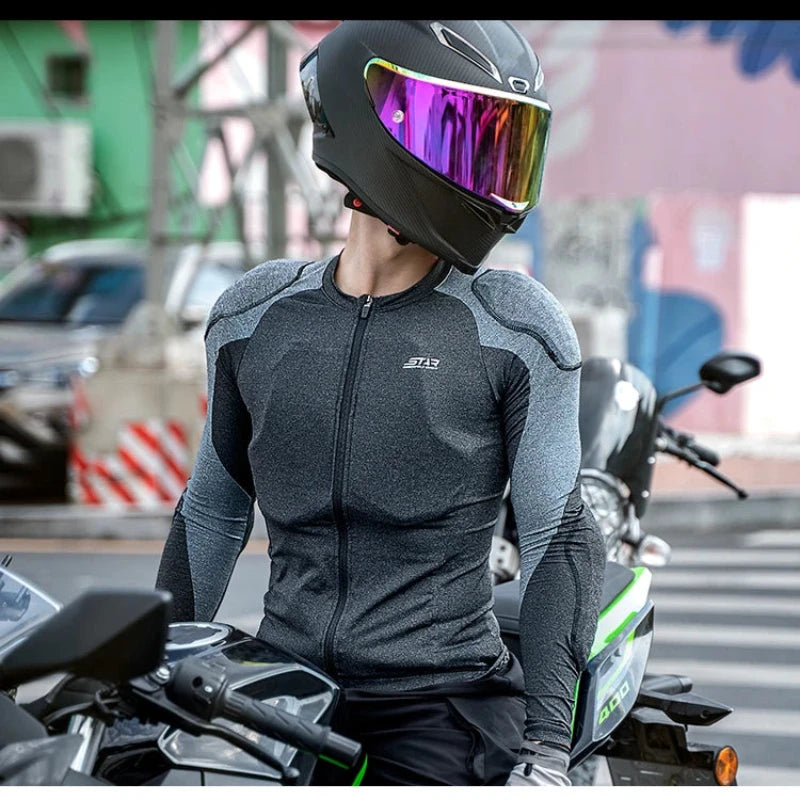 A person wearing a black full-face motorcycle helmet with a reflective visor and a dark gray long-sleeve zip-up riding jersey sits on a motorcycle in an outdoor urban setting.