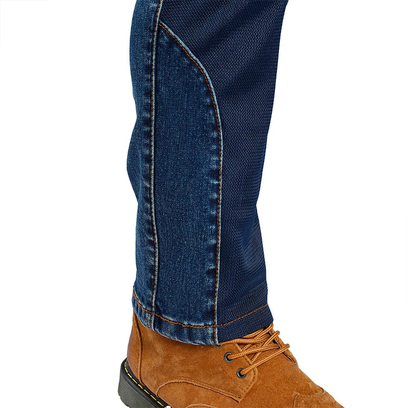 Close-up of a person's lower leg wearing dark blue denim jeans with contrast stitching and a brown suede lace-up boot, shown against a plain white background.