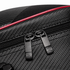 Close-up of a black textured bag with a red accent line and black zipper pulls on a white background.