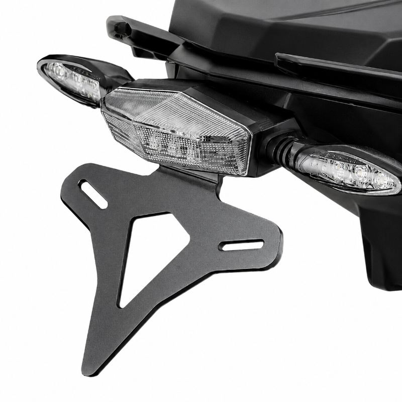A black metal motorcycle license plate frame shown mounted against the rear body of a black motorcycle, with the license light and side indicators visible, on a plain white background.