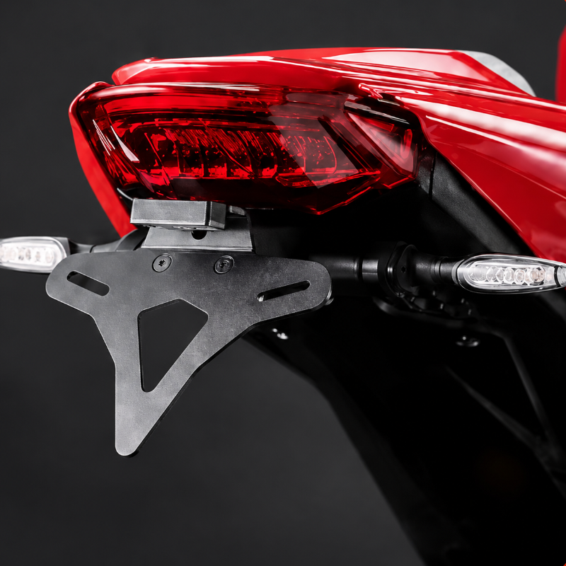 A matte black metal motorcycle license plate frame mounted on the rear of a red motorcycle, shown against a dark studio background.
