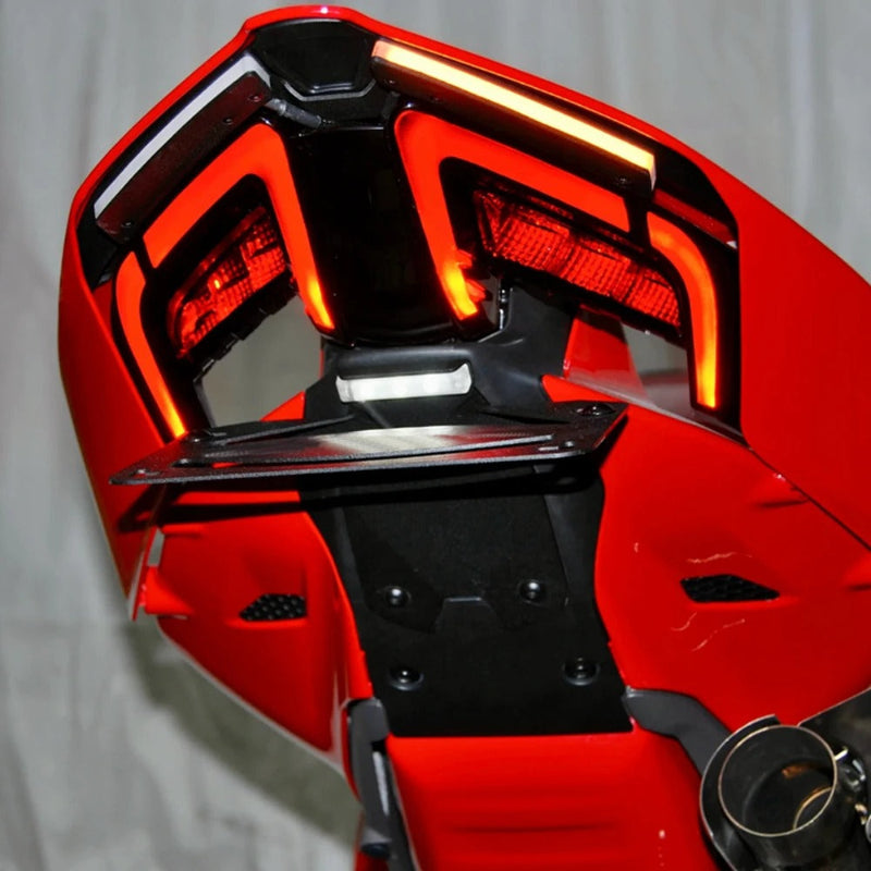 Close-up of a red motorcycle rear end showing the taillight assembly, rear spoiler, and exhaust pipe against a light gray backdrop.