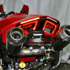 Close-up of a red motorcycle rear section showing the exhaust system with two large metallic mufflers and a black rear light assembly.