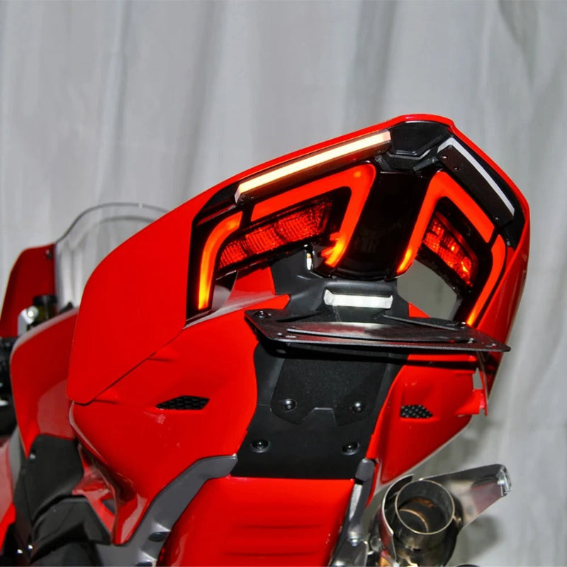 Close-up of a red motorcycle rear section showing the taillight assembly, rear spoiler, and exhaust against a light gray backdrop.