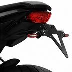Close-up of a black motorcycle license plate frame and mounting bracket attached behind a red taillight, shown on a white background.
