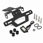 Black metal license plate frame kit with mounting hardware, including two black license plate frames, four black rubber bushings, four silver mounting bolts, two black washers, and a small rectangular LED light module with wiring, shown on a white background.
