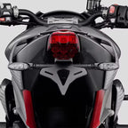 Close-up rear view of a sport motorcycle showing the black tail light assembly, red taillight, side indicators, and dark body panels with red accents against a light gray background.