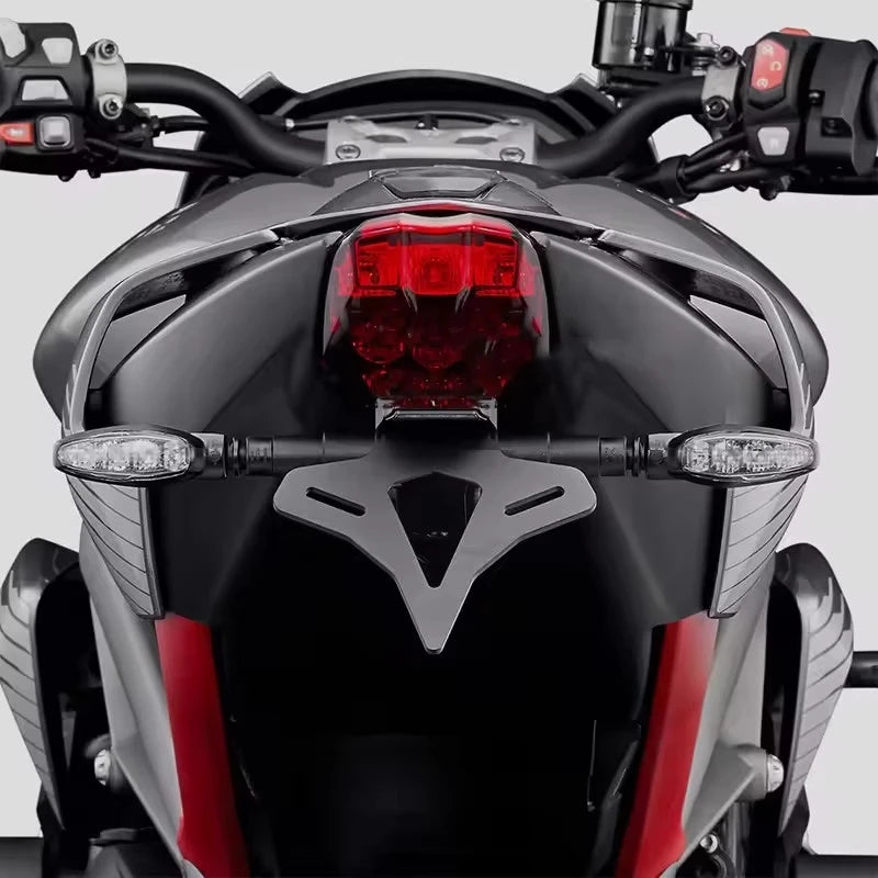 Close-up rear view of a sport motorcycle showing the black tail light assembly, red taillight, side indicators, and dark body panels with red accents against a light gray background.