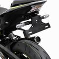 Close-up studio shot of the rear section of a black motorcycle, showing the license plate frame, side indicators, exhaust, rear tire, and a small yellow accent line on the wheel and bodywork against a white background.