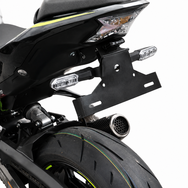 Close-up studio shot of the rear section of a black motorcycle, showing the license plate frame, side indicators, exhaust, rear tire, and a small yellow accent line on the wheel and bodywork against a white background.