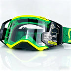 Green and neon yellow motocross goggles with a clear lens, featuring a black strap and a label that reads 'INCREASED IMPACT PROTECTION LENS LOCK'.