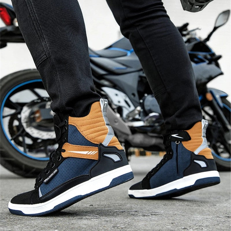 A person wearing black jeans and high-top sneakers with navy, orange, black, and white panels, standing next to a blurred motorcycle on a paved surface.