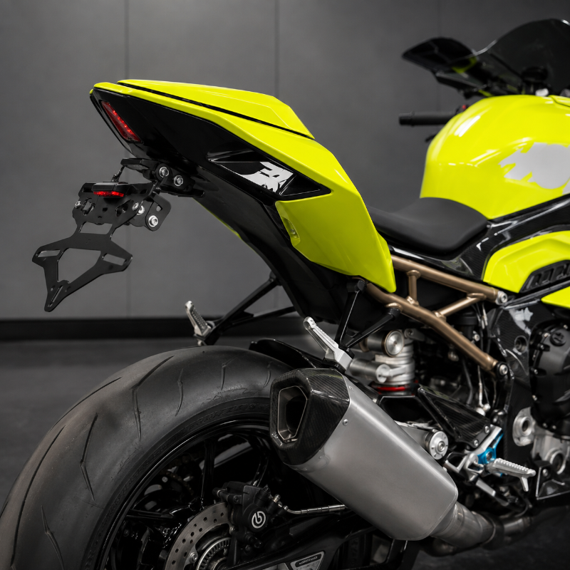 Close-up rear three-quarter view of a bright yellow and black sport motorcycle, showing the rear seat, black tail light assembly, black license plate frame, exhaust, and part of the fuel tank against a dark gray indoor studio background.
