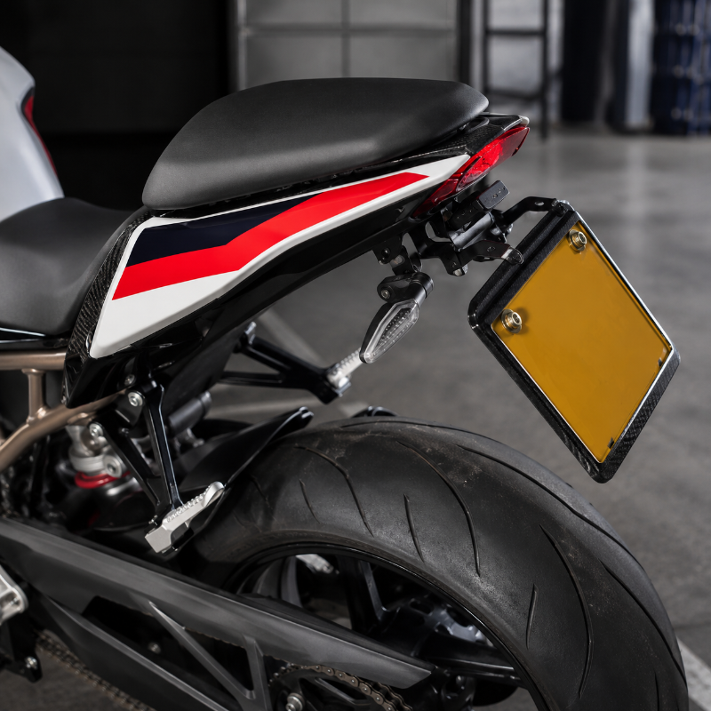 Close-up rear view of a motorcycle with a black seat, black body panels, red and white graphic stripes, a yellow license plate, and a black frame in an indoor setting.